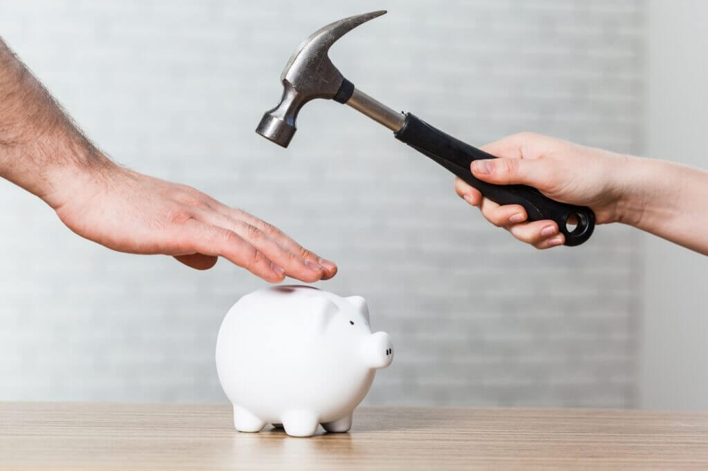 A hand holding a hammer which is raised above a white piggy bank